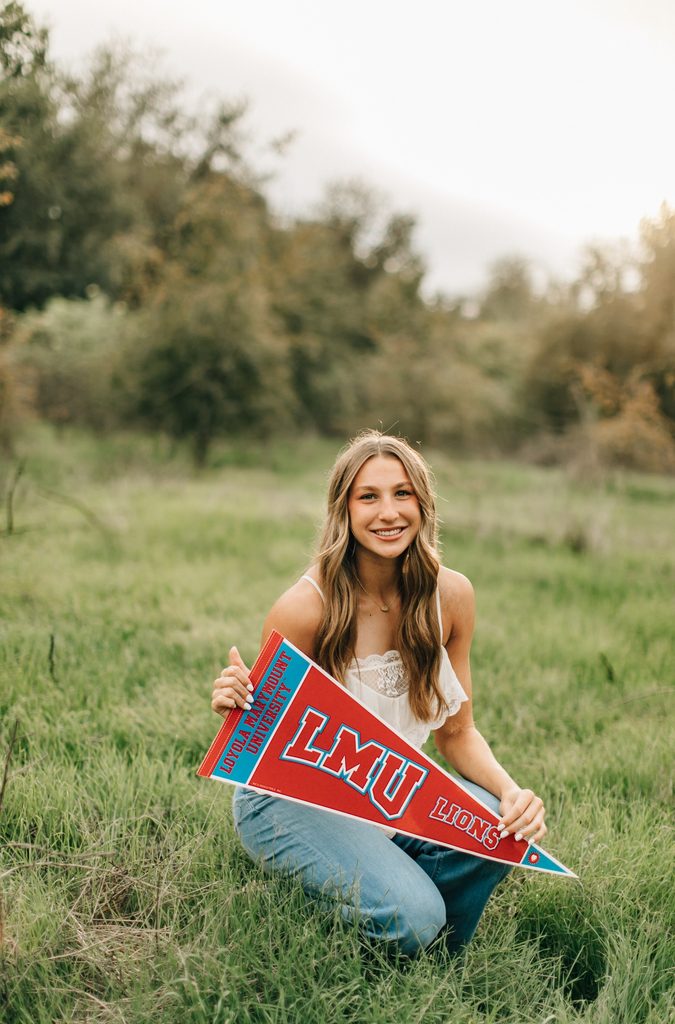 Female student holding LMU pendant in a field of grass